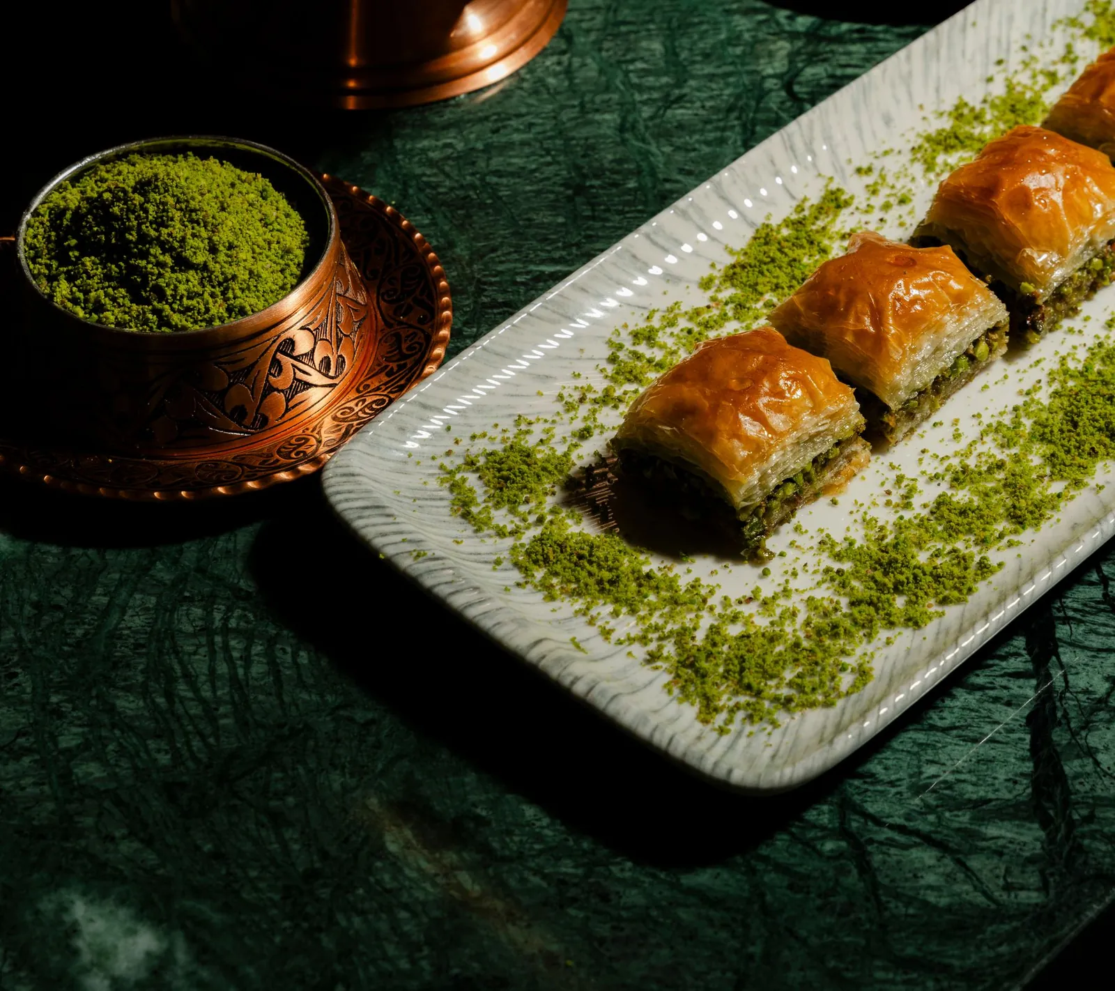 Pistazien-Baklava und eine Schale gemahlener Pistazien auf dunkelgrünem Marmor